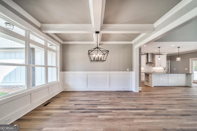 unfurnished dining area with beam ceiling, a wainscoted wall, light wood finished floors, and a decorative wall