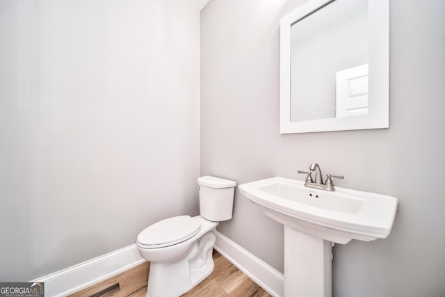 bathroom with toilet, wood finished floors, baseboards, and a sink