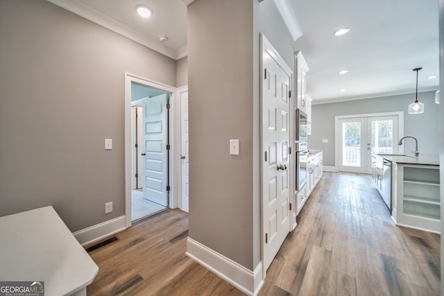 hall featuring crown molding, wood finished floors, visible vents, and baseboards