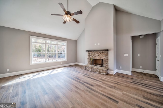 unfurnished living room featuring ceiling fan, baseboards, a stone fireplace, wood finished floors, and high vaulted ceiling