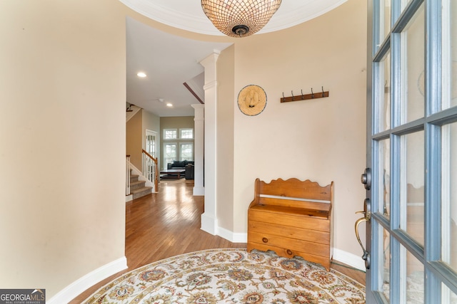 corridor featuring baseboards, stairway, wood finished floors, crown molding, and ornate columns