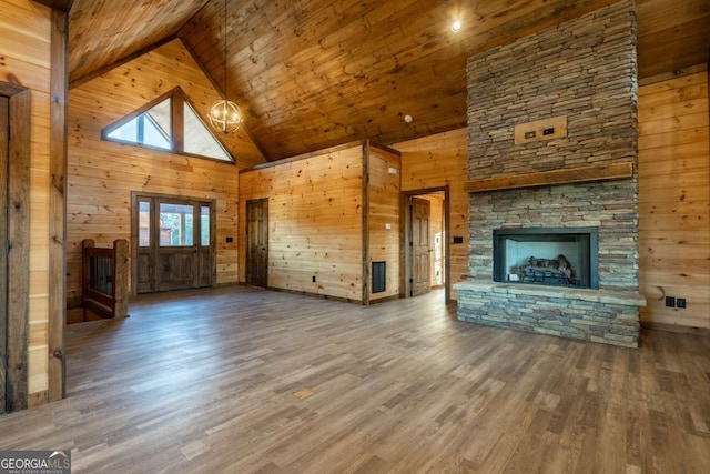 unfurnished living room with wood walls, wood finished floors, and a stone fireplace