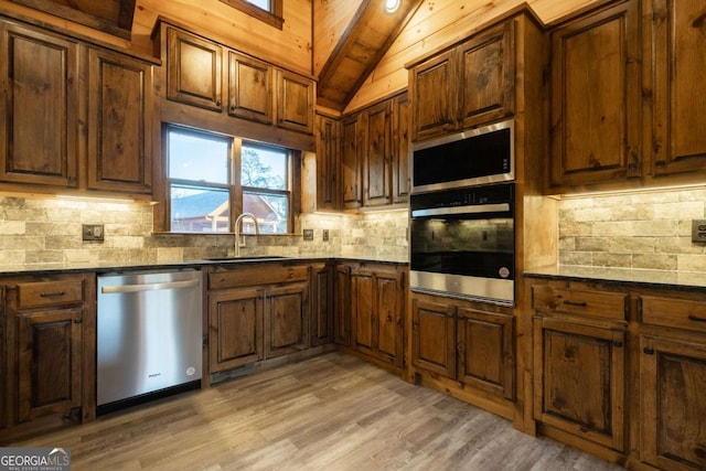 kitchen with tasteful backsplash, lofted ceiling, appliances with stainless steel finishes, light wood-style floors, and a sink