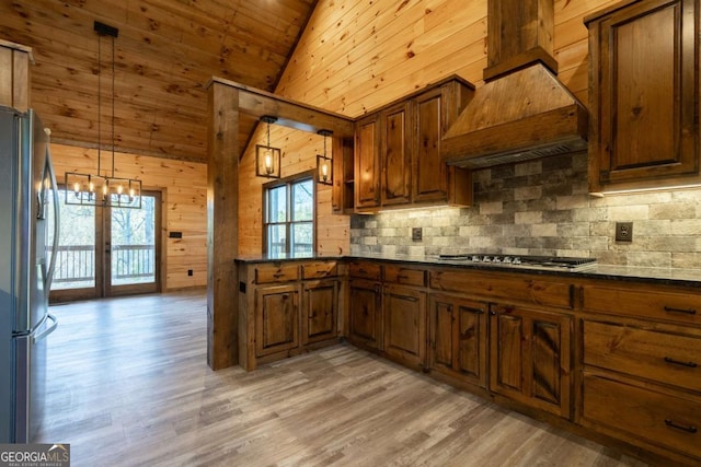 kitchen with light wood-style flooring, wooden walls, appliances with stainless steel finishes, custom exhaust hood, and dark countertops