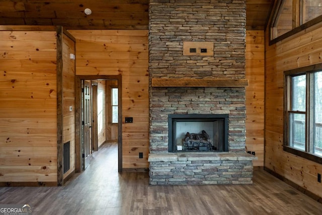 unfurnished living room with a towering ceiling, wooden walls, a fireplace, and wood finished floors