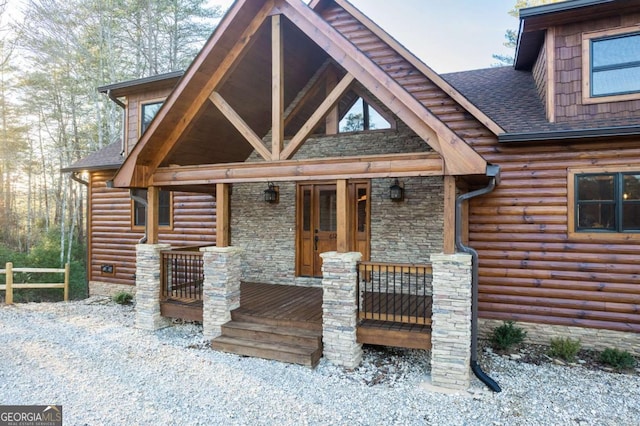 log cabin with a porch, faux log siding, stone siding, and a shingled roof