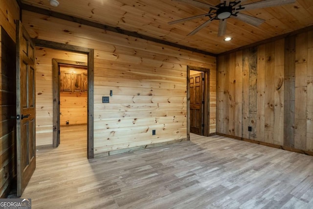 empty room featuring light wood-type flooring, wooden ceiling, ceiling fan, and wood walls