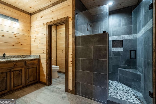 full bathroom with tiled shower, wood walls, vanity, and toilet