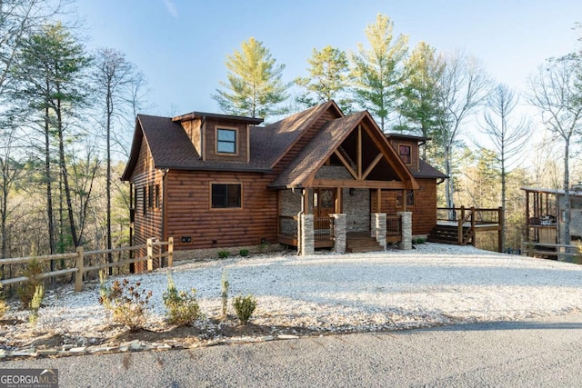 view of front of home featuring a shingled roof, faux log siding, fence, and a porch