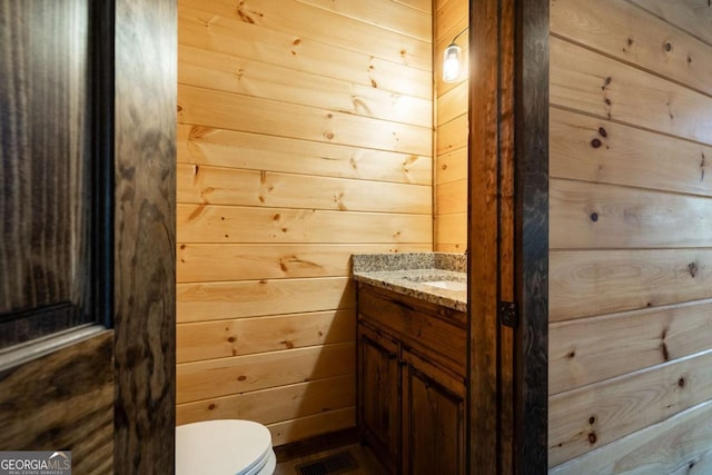 bathroom with visible vents, wooden walls, toilet, and vanity