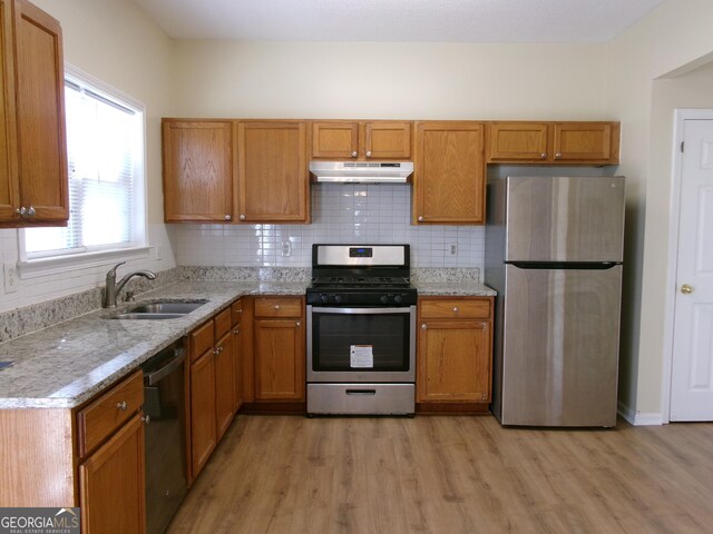 kitchen featuring under cabinet range hood, a sink, appliances with stainless steel finishes, light wood-type flooring, and tasteful backsplash