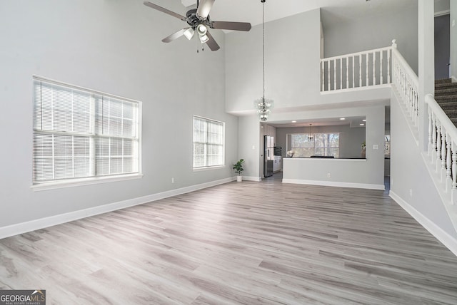 unfurnished living room featuring a towering ceiling, ceiling fan, wood finished floors, baseboards, and stairs