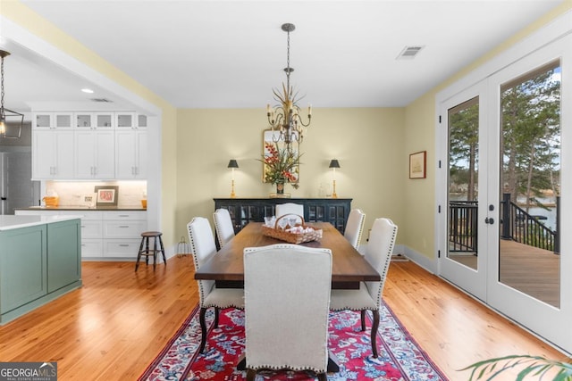 dining space with visible vents, baseboards, light wood-style flooring, an inviting chandelier, and french doors