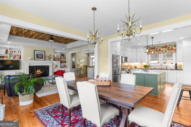 dining space with light wood finished floors, a lit fireplace, built in features, and a raised ceiling