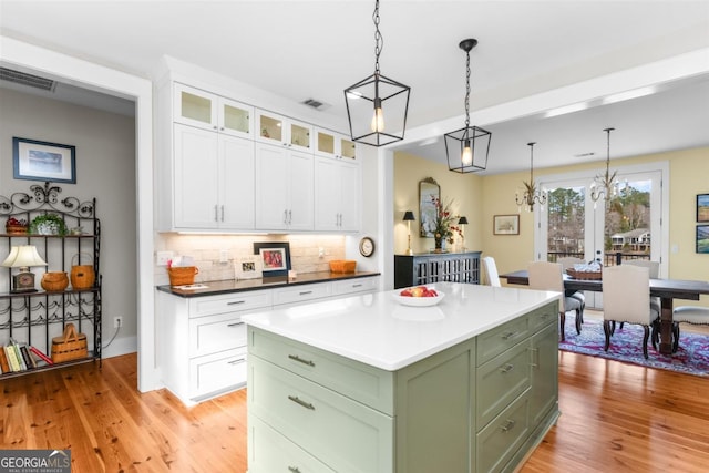 kitchen with visible vents, green cabinetry, light wood-style floors, white cabinetry, and backsplash