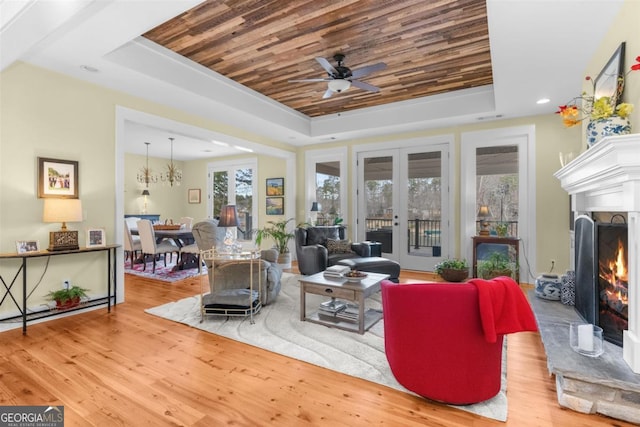 living room featuring a lit fireplace, a tray ceiling, wood finished floors, and french doors