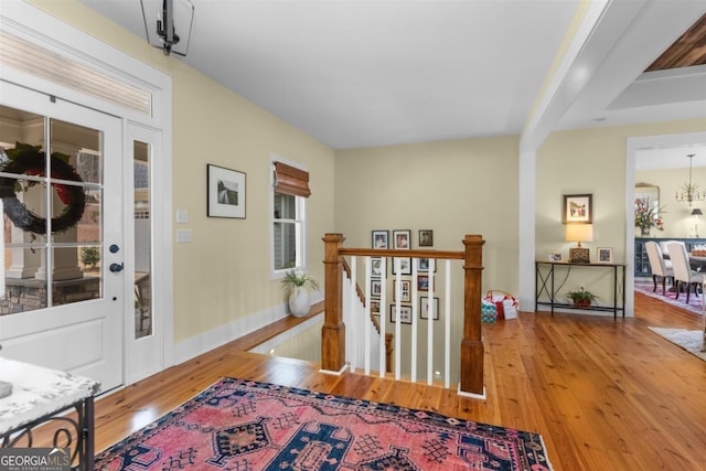 hall with an inviting chandelier, wood-type flooring, and an upstairs landing