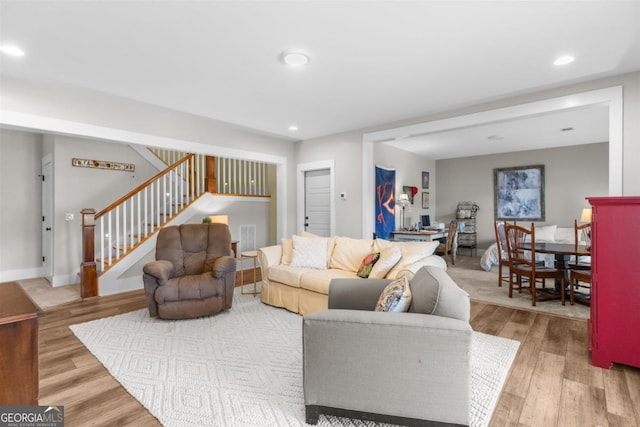 living room featuring stairs, baseboards, wood finished floors, and recessed lighting