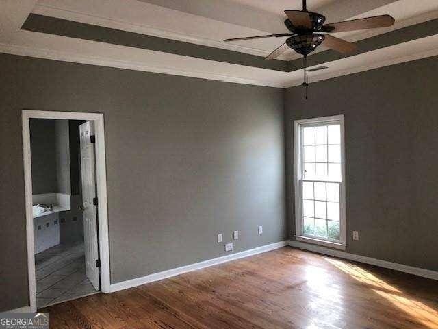 empty room featuring baseboards, wood finished floors, a raised ceiling, and crown molding