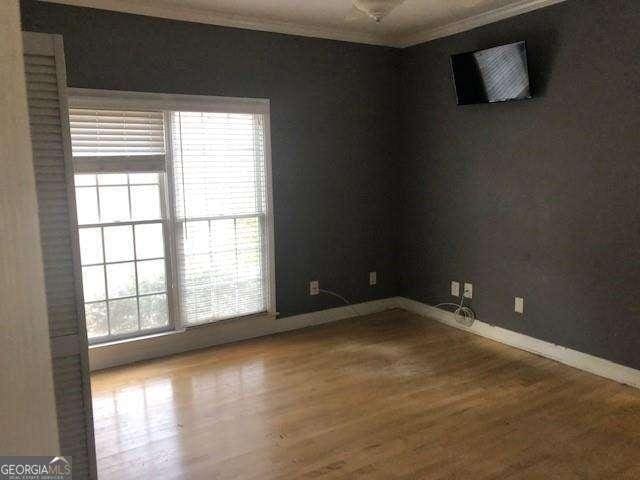 empty room with ornamental molding, wood finished floors, and baseboards