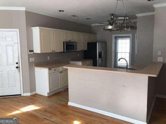 kitchen with appliances with stainless steel finishes, wood finished floors, a peninsula, light countertops, and crown molding