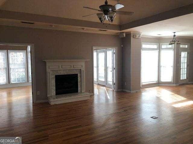 unfurnished living room with a ceiling fan, a raised ceiling, wood finished floors, and a high end fireplace