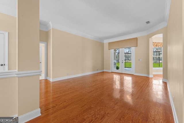 unfurnished living room featuring light wood finished floors, baseboards, arched walkways, and crown molding