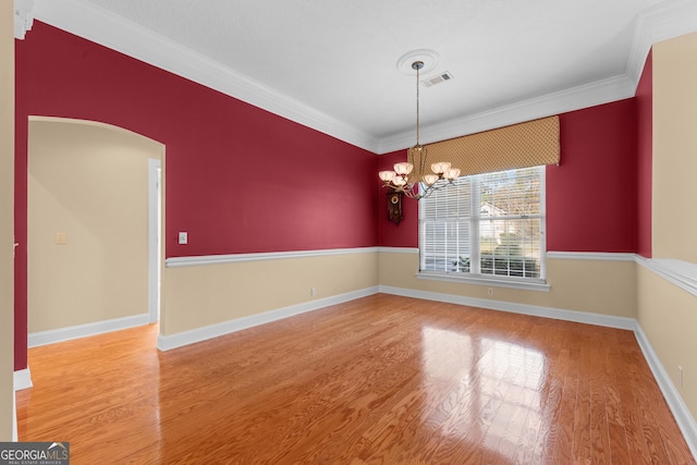 empty room with arched walkways, a chandelier, wood finished floors, visible vents, and crown molding