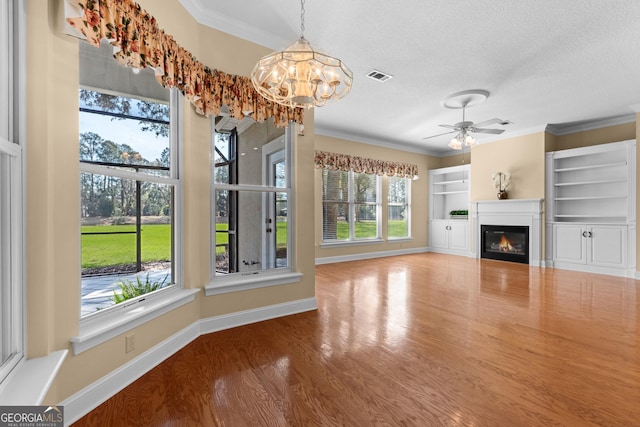 unfurnished living room featuring visible vents, ornamental molding, wood finished floors, and a glass covered fireplace