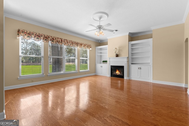 unfurnished living room featuring arched walkways, a ceiling fan, a glass covered fireplace, wood finished floors, and baseboards