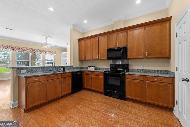 kitchen with brown cabinets, a peninsula, light wood-type flooring, black appliances, and a sink