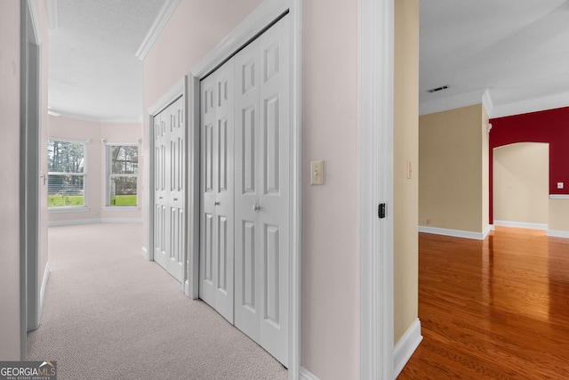 hallway with visible vents, baseboards, crown molding, and carpet flooring