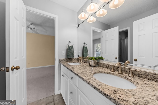 bathroom with a textured ceiling, double vanity, tile patterned flooring, and a sink