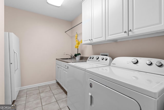 clothes washing area with light tile patterned floors, a sink, baseboards, washer and dryer, and cabinet space