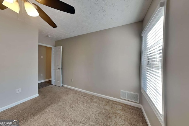 carpeted empty room with a healthy amount of sunlight, baseboards, visible vents, and a textured ceiling