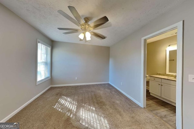 unfurnished bedroom with light colored carpet, a ceiling fan, a sink, a textured ceiling, and baseboards