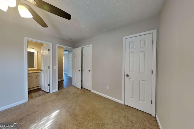 unfurnished bedroom with a textured ceiling, carpet floors, a ceiling fan, baseboards, and ensuite bath