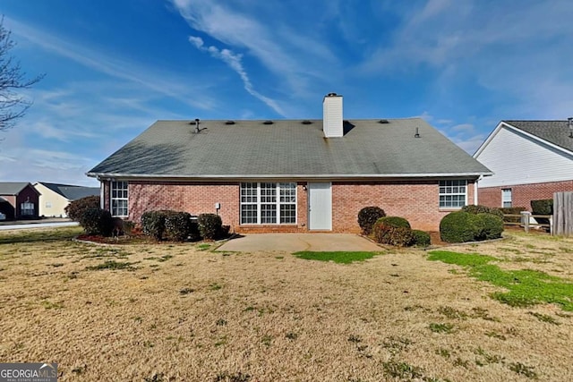 rear view of property featuring a yard, a patio area, a chimney, and brick siding