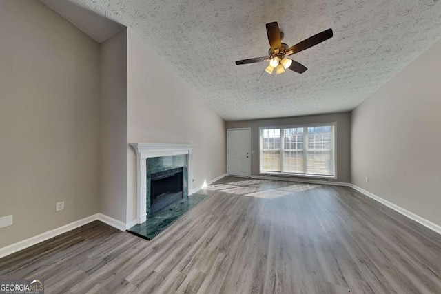 unfurnished living room with baseboards, a tiled fireplace, ceiling fan, wood finished floors, and a textured ceiling