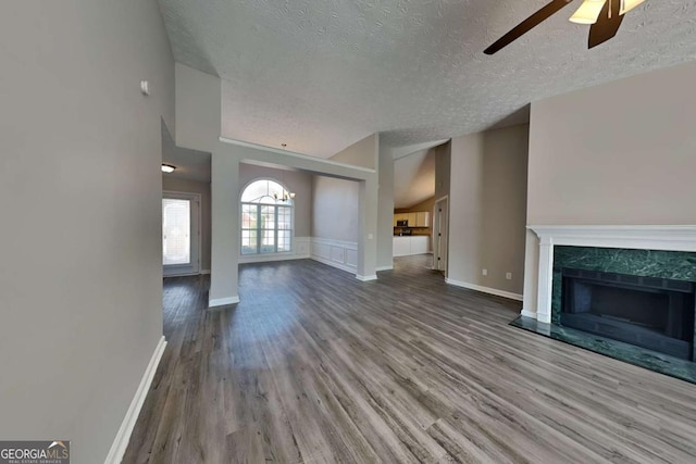 unfurnished living room featuring a textured ceiling, ceiling fan with notable chandelier, wood finished floors, a high end fireplace, and baseboards