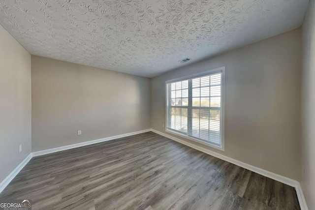 spare room featuring baseboards, a textured ceiling, visible vents, and dark wood-style flooring