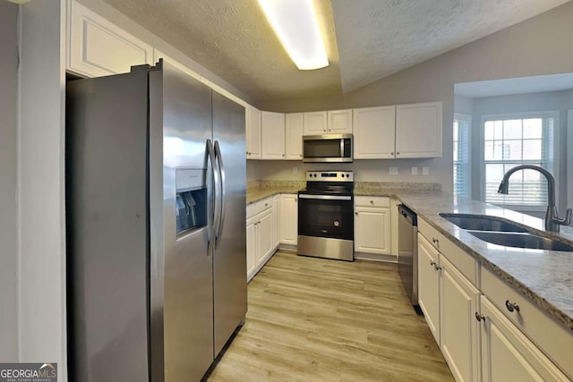 kitchen with light stone counters, a sink, light wood-style floors, vaulted ceiling, and appliances with stainless steel finishes