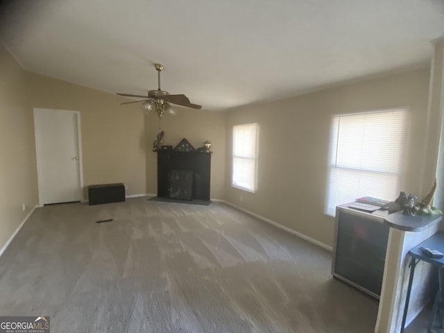 unfurnished living room featuring a fireplace with flush hearth, ceiling fan, carpet floors, and baseboards