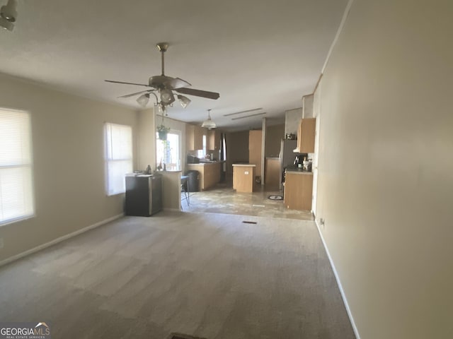 unfurnished living room featuring light carpet, a ceiling fan, and baseboards