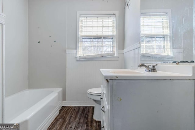 full bathroom featuring wainscoting, toilet, a tub, wood finished floors, and vanity