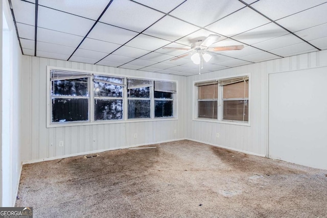 carpeted empty room featuring visible vents, a ceiling fan, and a drop ceiling