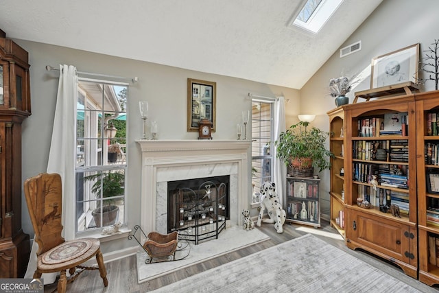 sitting room featuring visible vents, lofted ceiling with skylight, wood finished floors, a textured ceiling, and a fireplace