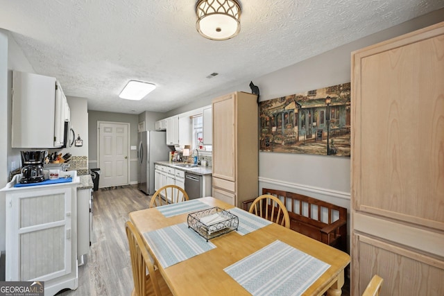 dining area with light wood-type flooring, visible vents, and a textured ceiling