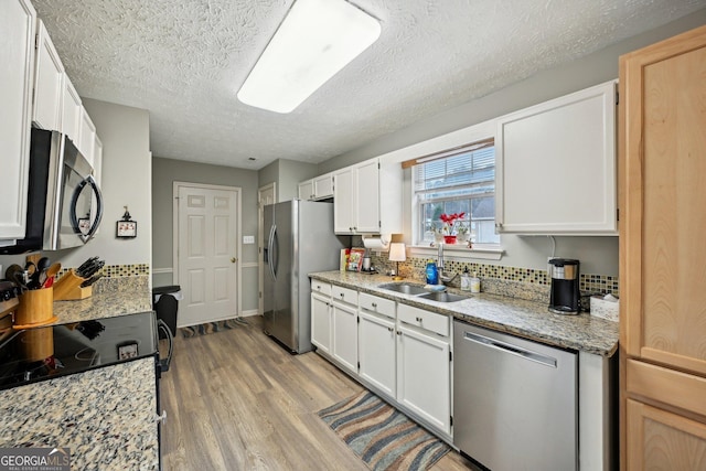 kitchen with stainless steel appliances, backsplash, white cabinets, a sink, and light wood-type flooring