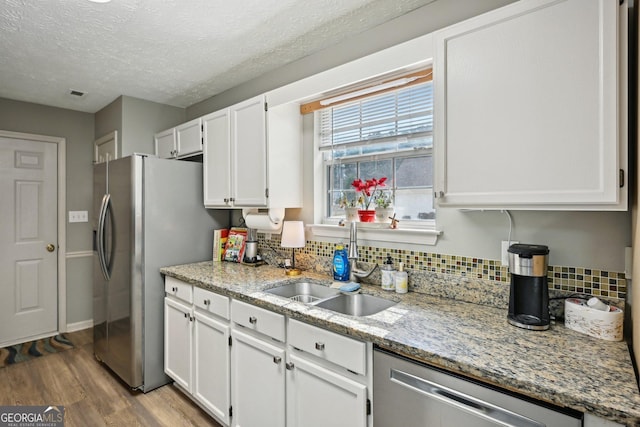 kitchen featuring tasteful backsplash, stainless steel appliances, wood finished floors, white cabinetry, and light stone countertops